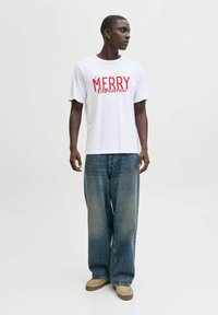 Bílý bavlněný tričko s červeným textem "MERRY Christmas". V kombinaci s volnými modrými džíny a béžovými nazouvacími botami. Jednoduchý design.