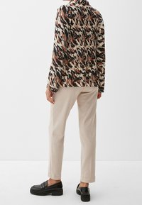 Blusa con stampa animale caratterizzata da una combinazione di colori neri, beige e ruggine; maniche lunghe; retro plissettato; abbinata a pantaloni beige e mocassini neri.