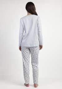 Top gris de manga larga con escote redondo, combinado con pantalones de pijama gris claro que presentan un patrón a rayas y pequeños motivos de corazones coloridos.