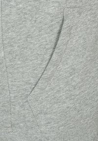 Grå sweatshirttyg med en något texturerad yta; har en framficka och kontrasterande sömmar längs kanterna.