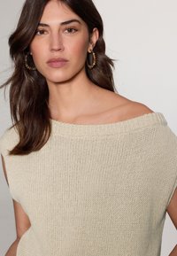 Lichtbeige gebreide trui met een off-shoulder decolleté, geribde randen en korte mouwen. Opvallende textuur en een losse pasvorm.