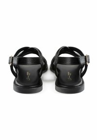 Sandali neri in pelle con design a fascia incrociata, cinturino alla caviglia regolabile e suola piatta. Presentano dettagli minimi e una texture liscia.