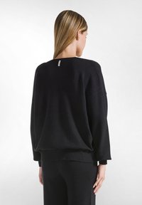Maglione nero oversize con colletto rotondo, polsini e orlo a coste. Realizzato in tessuto morbido con un'etichetta minimale sul retro.