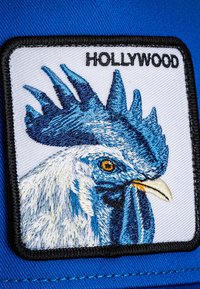 Embroidered patch featuring a blue and white rooster's head with a golden eye, outlined in black, with "HOLLYWOOD" above, on a blue background.