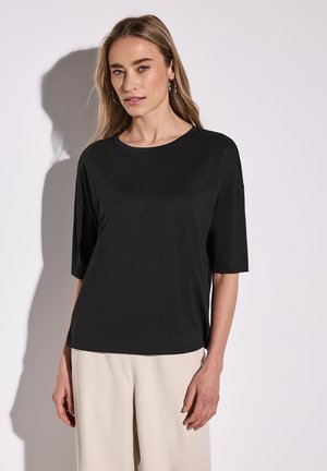 Haut noir à manches courtes avec un col rond et une coupe décontractée, fabriqué dans un tissu doux. Porté avec un pantalon large de couleur claire.