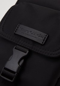 Borsa in tessuto nero caratterizzata da una superficie liscia, chiusura con fibbia in plastica e un'etichetta rettangolare in pelle impressa con "Marc O'Polo."