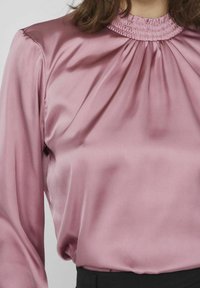 Långärmad blus i mjukt, satinliknande tyg, ljusrosa med rynkad halsringning och svävande siluett. Svart midjeband nedanför.