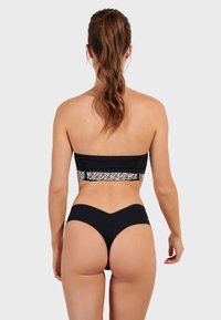 Čierny bandeau plavkový top s vzorovaným pásom a zodpovedajúcimi čiernymi vysokými spodkami. Hladká textúra, minimalistický dizajn a tesný strih.