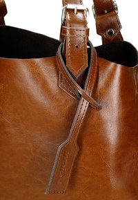 Hnědá kožená taška přes rameno s dvojitými úchyty, zapínáním na přezku a prošitým koženým štítkem s raženým detailem "wooloo".