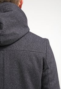 Giacca grigia in misto lana con cappuccio, caratterizzata da una texture liscia e un design della schiena strutturato. Mostra cuciture e dettagli di impuntura.