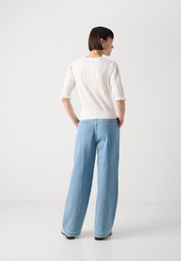 Maglione bianco a coste con maniche voluminose; abbinato a jeans a gamba larga blu chiaro. Design semplice, texture morbida e linee pulite.