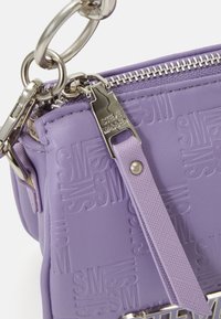 Sac en lavande Steve Madden avec motif en relief "SM", fermeture éclair argentée et tirette de fermeture éclair texturée assortie en lavande avec rivet métallique.