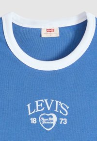 Синя тениска Levi's с бяла яка и бял печатен текст "Levi's 1873 True Denim" във формата на сърце отпред.