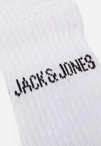 Hvide bomuldsokker med ribbet tekstur og mærkenavnet "JACK & JONES" trykt med fede sorte bogstaver.