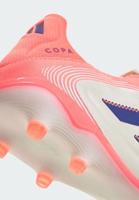 Botín de fútbol rosa con una parte superior texturizada, que presenta una suela blanca y tacos naranjas. Marca "COPA" en púrpura en el talón.