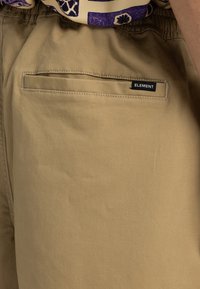 Pantalones cortos caqui con un bolsillo trasero que lleva una etiqueta negra de "ELEMENT", confeccionados en una suave y texturada mezcla de algodón.