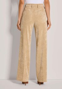 Beige Cordhosen mit weitem Bein, vertikaler Rippstruktur, hoher Taille und zwei Gesäßtaschen. Glatte Textur.