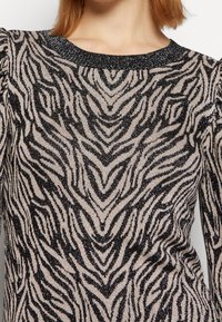 Top a maniche lunghe nero e beige con motivo a strisce zebrate. La texture scintillante e il collare nero accentuano il design.