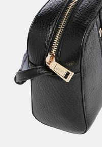 Czarna torebka o fakturowanej powierzchni ze złotym zamkiem błyskawicznym i znakowanymi okuciami. Posiada usztywniony kształt oraz krótki pasek ułatwiający noszenie.