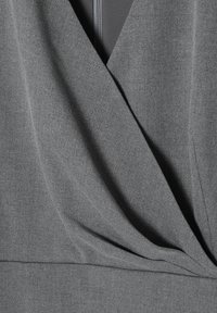 Grått tygtop med design i V-ringning, som har draperad textur och veck. Dragkedjestängning på baksidan för funktionalitet.