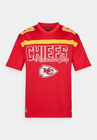 Piros hálós mez sárga díszítéssel, fehér betűkkel "CHIEFS" és "Kansas City" felirattal. Az elején csapatlogóval és a vállakon számmal.