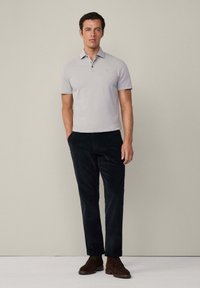 Světle šedá polo tričko s třemi knoflíky, spárované s černými kordovými kalhotami. Hnědé semišové boty dokončují outfit. Jednoduchý, přiléhavý design.