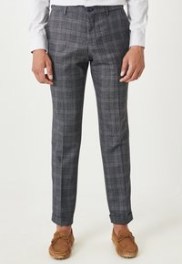 Ciemnoszare spodnie w kratę o dopasowanym kroju, z delikatną teksturą i podwiniętymi nogawkami. Połączone z jasnobrązowymi butami typu mokasyny.