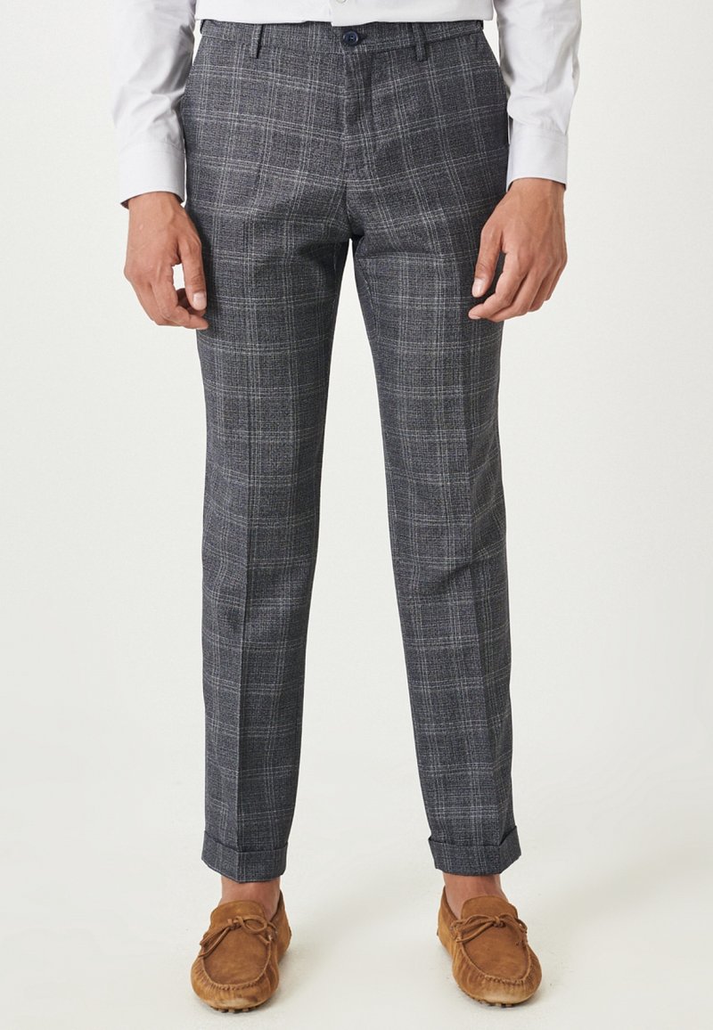 Ciemnoszare spodnie w kratę o dopasowanym kroju, z delikatną teksturą i podwiniętymi nogawkami. Połączone z jasnobrązowymi butami typu mokasyny.