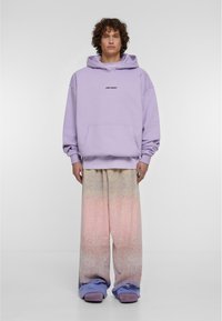 Lavandas pārāk liels kapuce ar priekšējo kabatu un drukātu tekstu. Brīvi, nolaišanās sporta bikses ar pāreju no pasteļrozā līdz zilu pie potītēm.