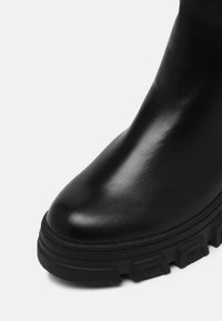 Black leather ankle boot with a glossy finish, rounded toe, and thick rubber sole featuring textured treads for grip.