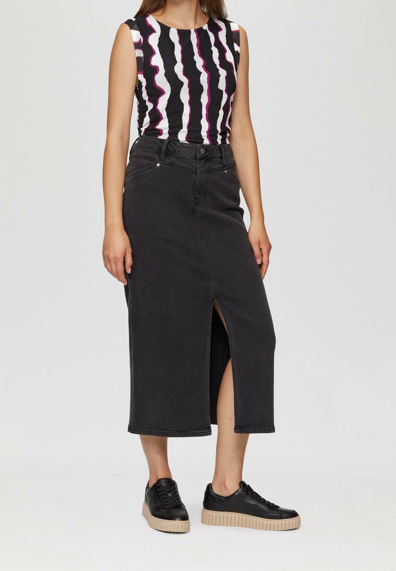 Femme portant un haut sans manches noir et blanc à motifs, une jupe midi noire taille haute avec une fente devant, et des baskets à plateforme noires.