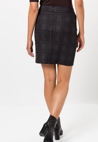 Falda de cuadros oscuros con un corte entallado, que presenta una cinturilla plana y cremallera trasera. Combinada con botas de tacón negras hasta el tobillo.