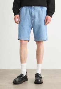 Shorts in denim azzurro chiaro con vestibilità rilassata, orli risvoltati e chiusura con bottone. Abbinati a mocassini neri e calze bianche a coste.