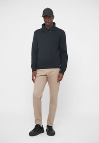 Merihenkinen neulepusero, jossa on kaulus, beiget housut ja mustat lenkkarit. Asusteena musta lippis. Yksinkertainen ja moderni muotoilu.