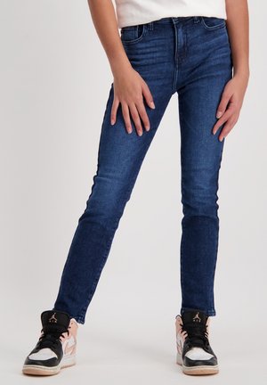 Slim-fit, dark blue denim jeans with a faded design, featuring five pockets and a classic waistband, paired with black and pink sneakers.