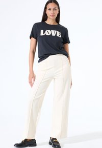 Zwarte T-shirt met 'LOVE' grafiek, crème wijde broek, en zwarte instappers. Glad materiaal, relaxte pasvorm en duidelijke naden op de broek.