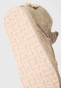 Scarpa in tela blu con suola in gomma ruvida di colore bianco sporco, caratterizzata da scritte in rilievo e una rifinitura in juta intrecciata lungo il bordo. Si nota un aspetto usurato.