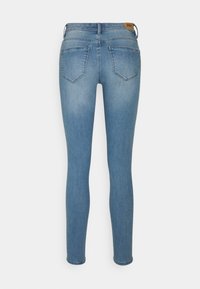 Uske traperice, svijetlo plavi denims, imaju dva stražnja džepa, srednje visok pojas i kožni logotip iznad desnog džepa.