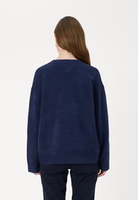 Maglione lavorato a maglia di colore blu scuro con una vestibilità comoda, caratterizzato da un orlo e maniche a costine. La texture appare morbida e leggermente pelosa.