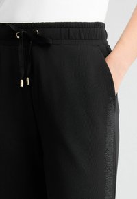 Pantalons de jogging noirs en tissu doux, dotés d'une taille élastique avec cordon de serrage et d'une bande décorative sur le côté.