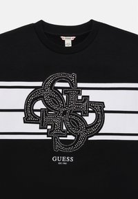 Sweatshirt noir avec des rayures blanches, présentant un design de logo orné de strass au centre. Coupe classique à col rond.