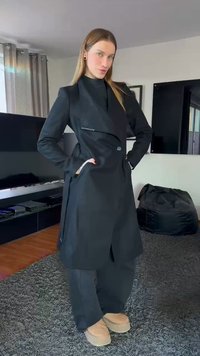 Casaco preto com um design estruturado, frente dupla abotoadura e grandes lapelas. Combinado com calças pretas e calçado de cor clara.