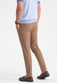 Cienkie spodnie slim-fit w kolorze beżowym z bocznymi kieszeniami, w połączeniu z brązowymi zamszowymi loafersami. Jasnoniebieski sweter z krótkim rękawem z akcentami w prążki.