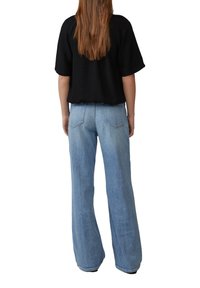 Haut noir à manches courtes avec une coupe décontractée, porté avec un jean large bleu clair, présentant des poches arrière standard et une texture en denim lisse.