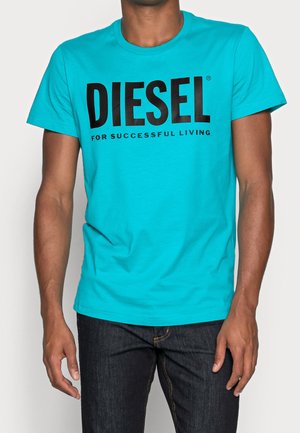 Uomo che indossa una maglietta blu brillante con un grande testo nero "DIESEL" e un testo più piccolo "FOR SUCCESSFUL LIVING," abbinata a jeans scuri.