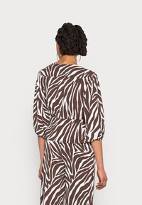 Blusa de padrão zebra castanho e branco com mangas bufantes, textura suave e cintura ajustada. A vista traseira mostra a continuidade do decote e do padrão.