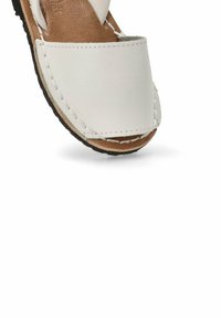 Sandalia de cuero blanco con puntera redondeada, plantilla de cuero marrón y suela de goma negra. Presenta detalles de costura a lo largo de los bordes.