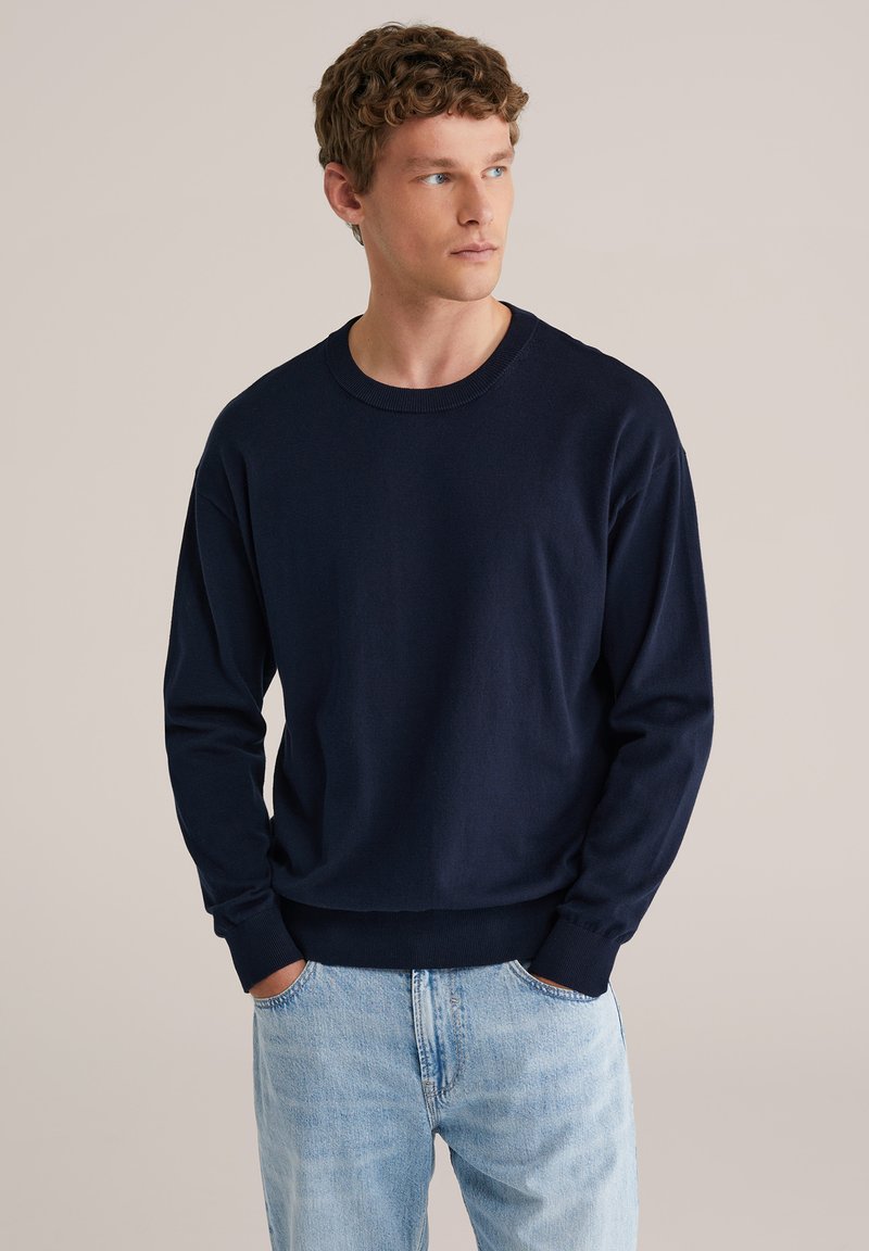 Sweat-shirt bleu marine à manches longues avec un col rond, des poignets et un ourlet côtelés, fabriqué en tissu doux, associé à un jean bleu clair.