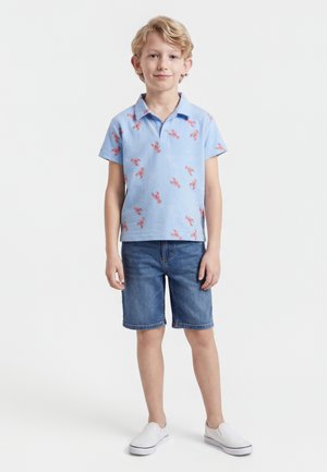 Young boy standing wearing a light blue lobster print polo, denim shorts, and white slip-on shoes against a white background.