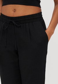 Sorte joggebukser med elastisk midjebånd, har to sidelommer og et teksturert stoff. Enkel, rett ben design.